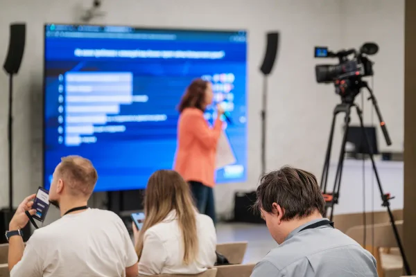 Presentatie voor een groot scherm met live pollresultaten, opgenomen met een camera op statief zodat het webinar terug te kijken is.
