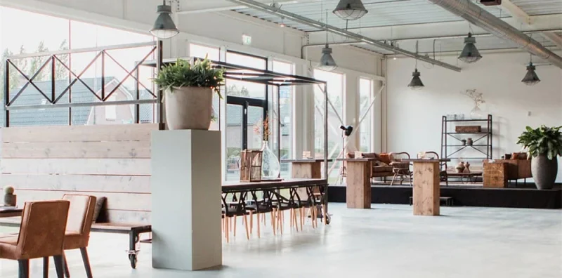 Lichte loftruimte met houten trap, planten en losse zitplekken.