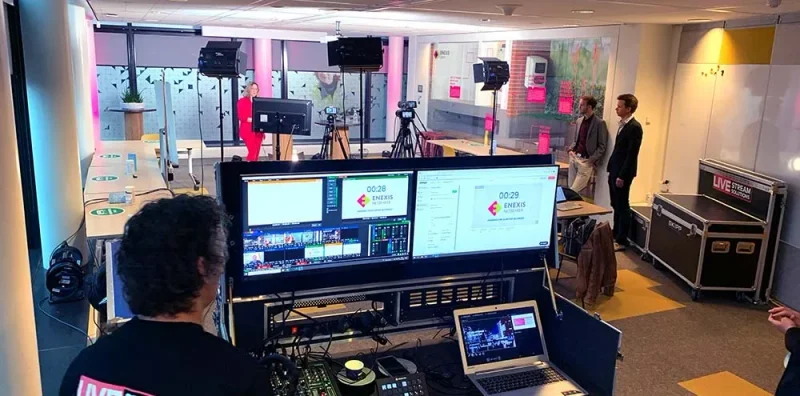 Technicus achter de regie met multiviewmonitoren, tijdens een uitzending op kantoor.
