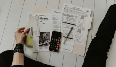 Iemand werkt met formulieren en een rekenmachine aan een kostenoverzicht.
