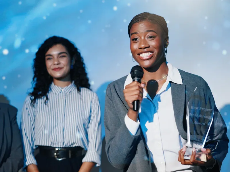 Winnaar met microfoon en award op het podium van een awardshow, in blauw licht.