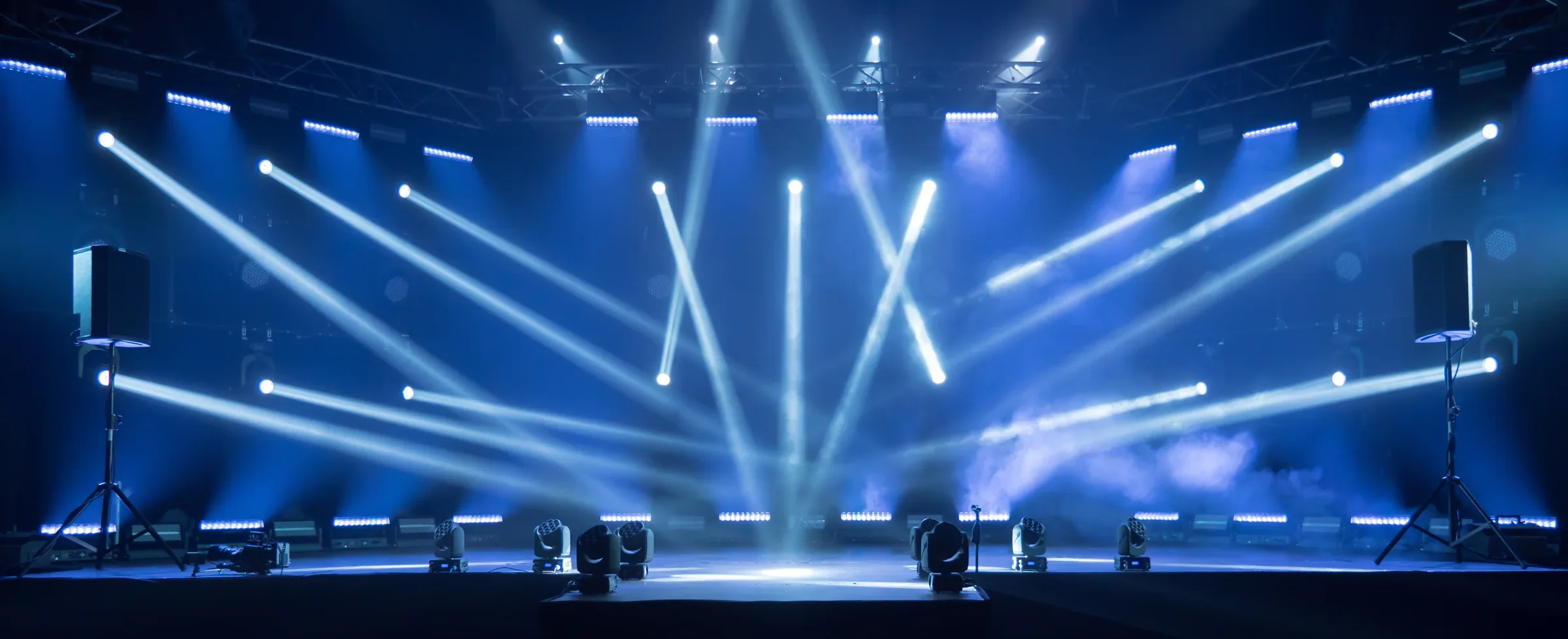 Leeg podium met blauwe lichtbundels en een groot scherm, klaar voor de start van een live event.