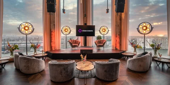 Talkshowdecor met loungestoelen en een LED-scherm voor panoramische ramen met uitzicht over Amsterdam.