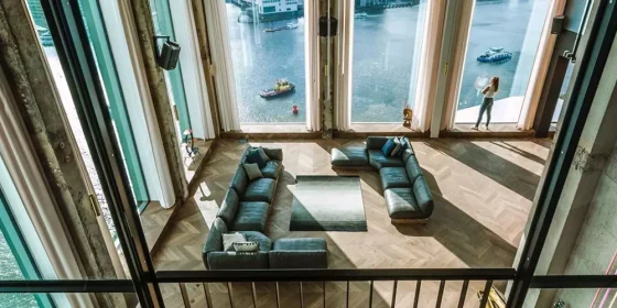 Loungehoek met banken voor manshoge ramen met uitzicht over het water.
