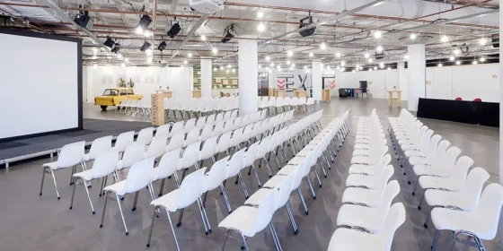 Lege zaal met rijen witte stoelen voor een groot projectiescherm.