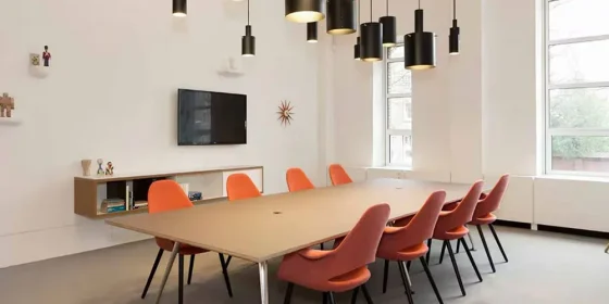 Vergaderruimte met een lange tafel en oranje stoelen.