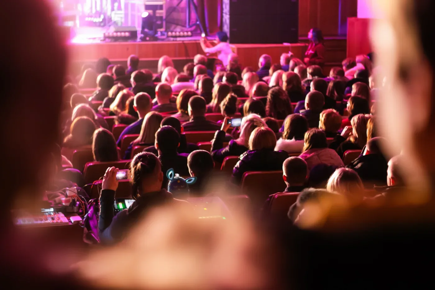 Volle theaterzaal in rood en paars licht tijdens een optreden, gezien vanaf het balkon.