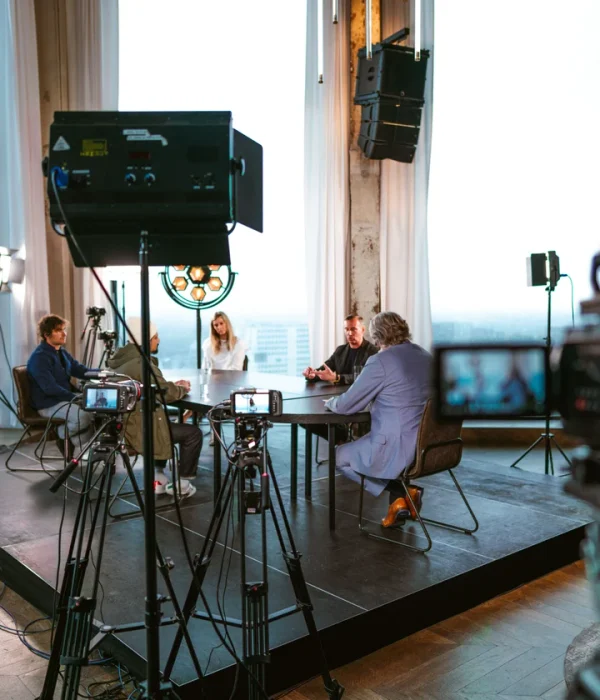 Overzicht van de set met camera op statief, studiolampen en het gesprek aan tafel.