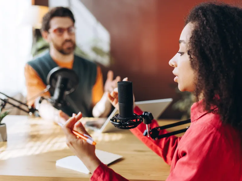 Twee gesprekspartners met microfoons aan tafel tijdens een inhoudelijk interview.