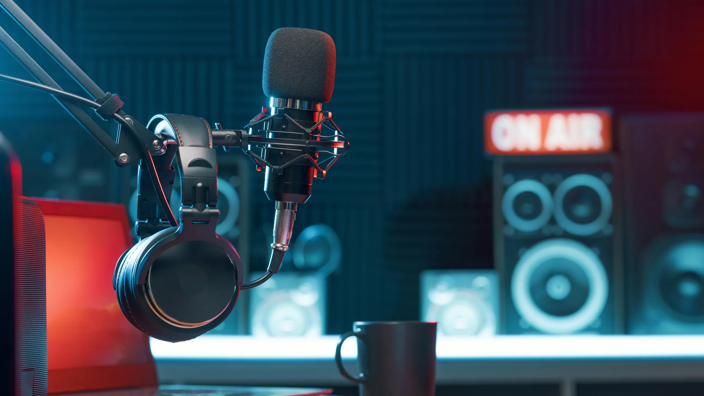 Studiomicrofoon met koptelefoon aan de arm, voor een ON AIR bord en studiomonitoren in een blauw uitgelichte podcaststudio.