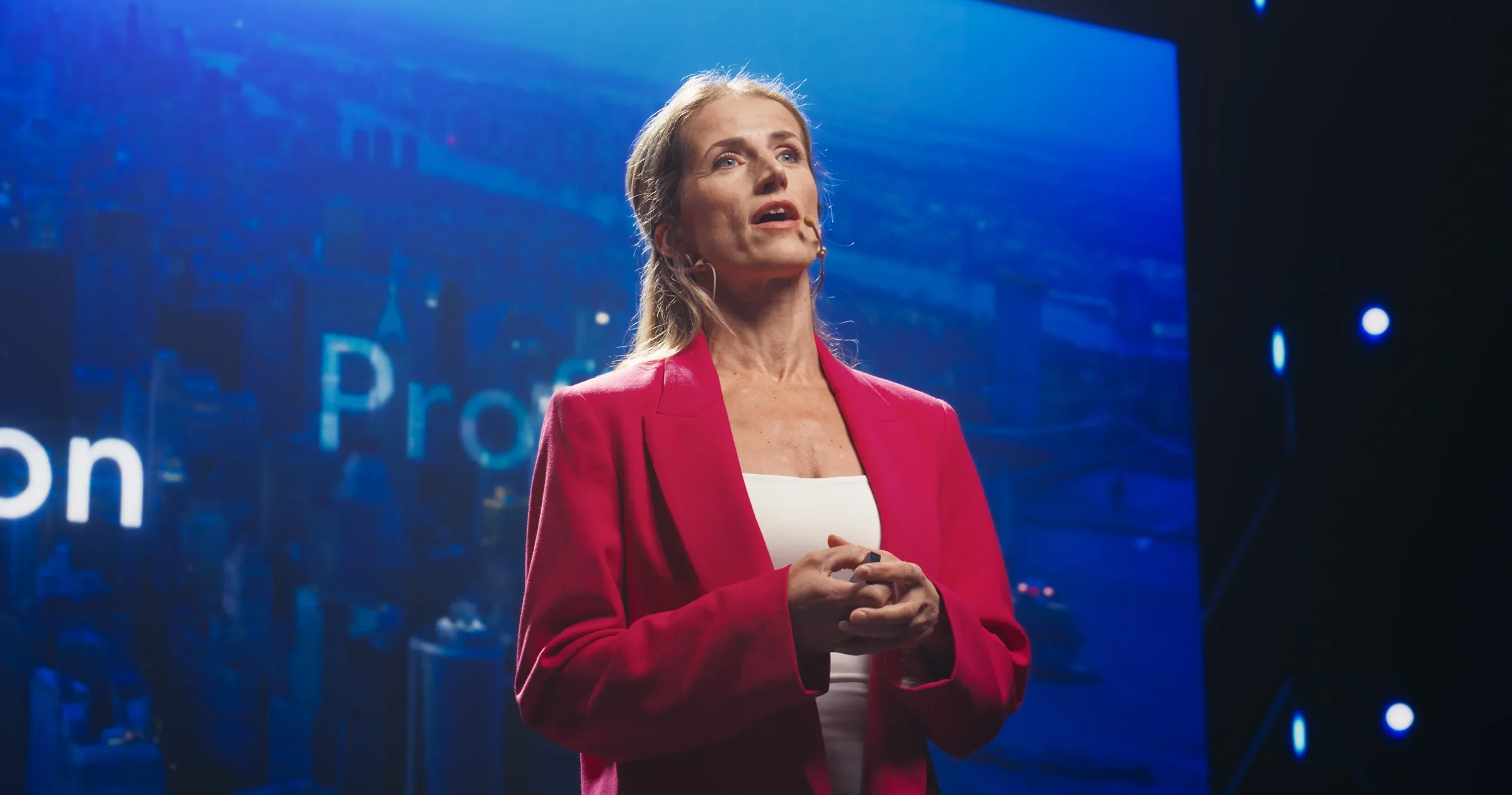 Spreker op een podium voor een groot scherm tijdens de presentatie van een nieuw product.