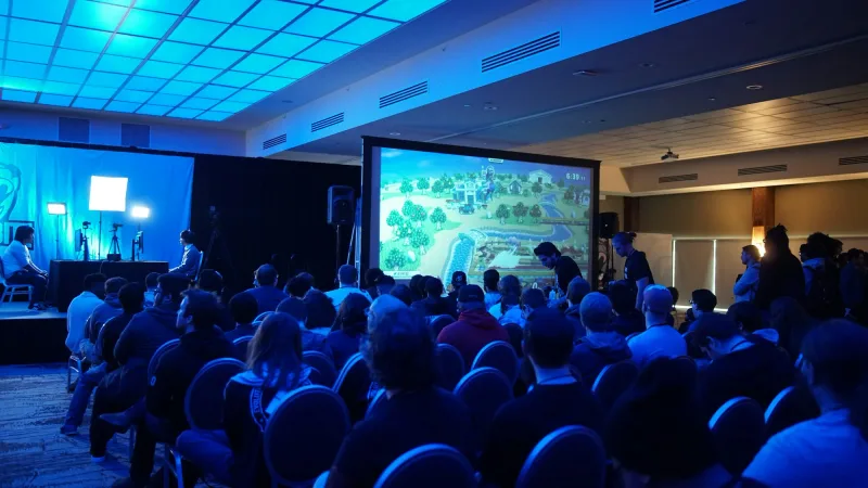 Publiek in een blauw uitgelichte zaal kijkt naar een groot presentatiescherm.