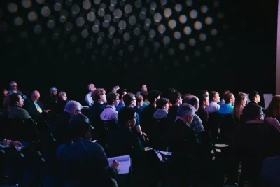 Publiek in een verduisterde zaal kijkt naar het podium tijdens een grote productie.