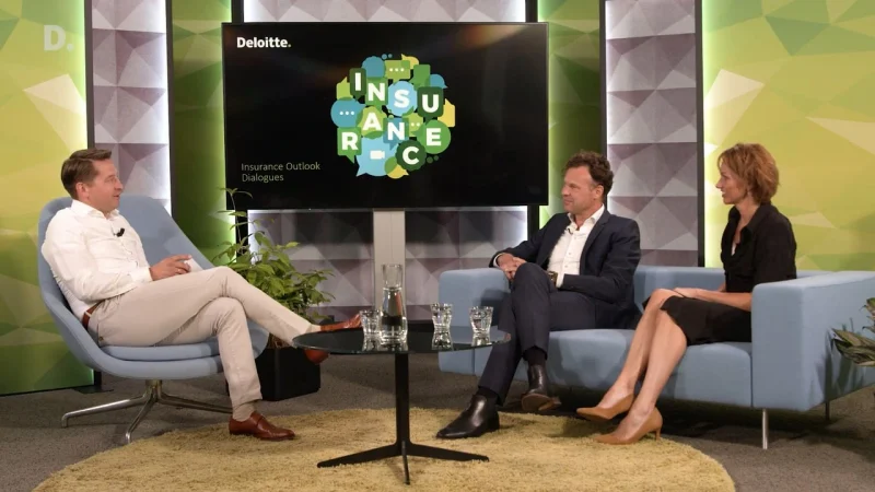 Talkshowopstelling met een gespreksleider en twee gasten in fauteuils, voor een scherm met de titel Insurance Outlook Dialogues.