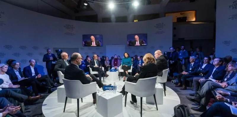 Paneelgesprek op een podium met publiek in de zaal en de sprekers op grote schermen.