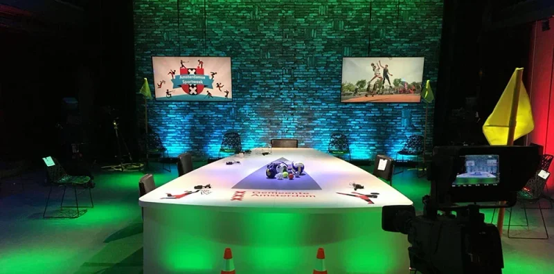 Studio met een verlichte tafel, schermen en decor, klaar voor een uitzending.