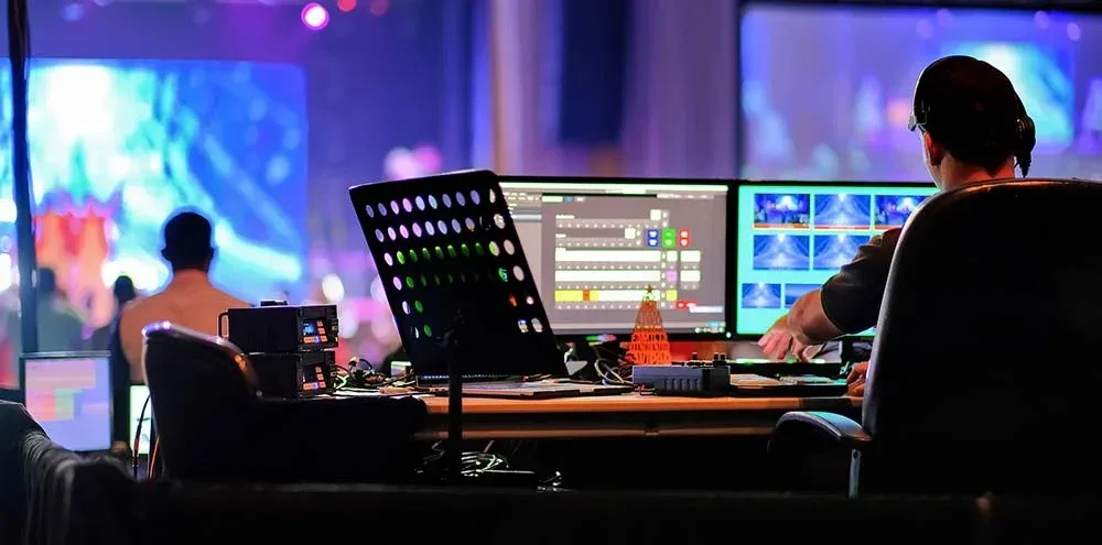 Technicus bedient de mengtafel achter de monitoren tijdens een live uitzending.