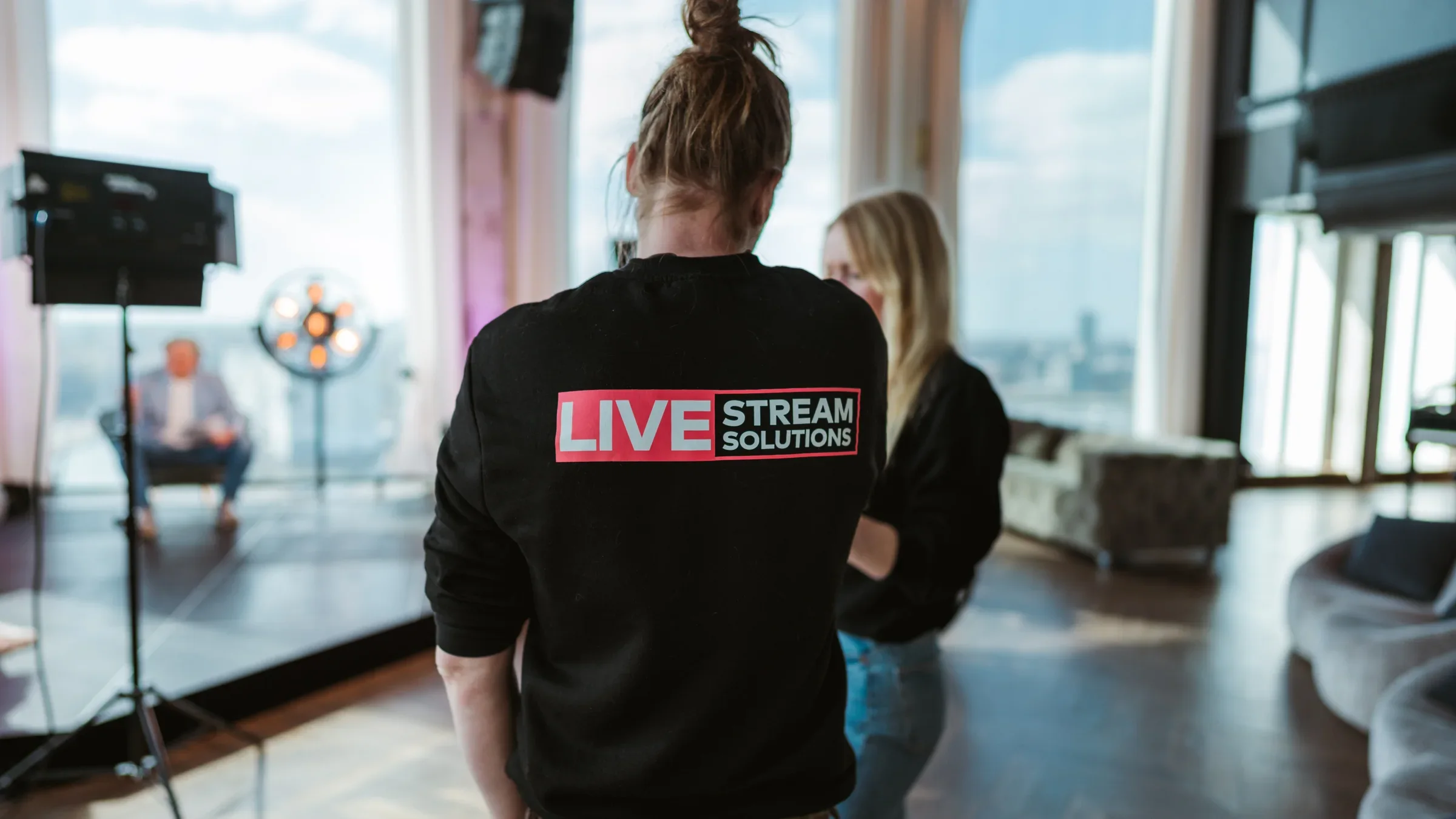 Crewlid van Livestream Solutions kijkt toe bij een studioset op kantoor, waar een spreker voor de camera staat.
