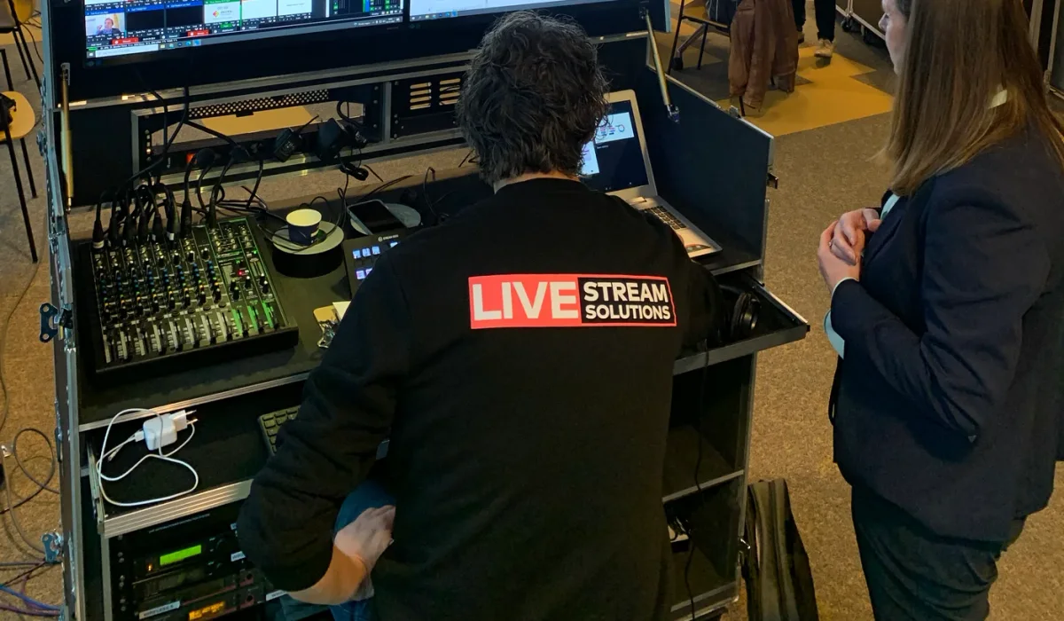 Technicus van Livestream Solutions bedient de regie achter twee monitoren en een geluidstafel, op locatie bij de klant.