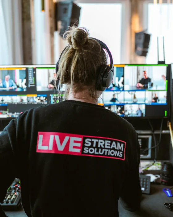 Crewlid van Livestream Solutions met koptelefoon achter de regie, met multiviewmonitoren van de uitzending in beeld.